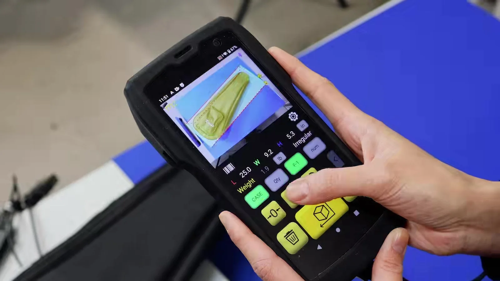 The M2 in an operator's hands after scanning a soft padded bag: the bag outlined with its bounding box on the photo, L 25.0, W 9.2, H 5.3 in, and the shape Irregular