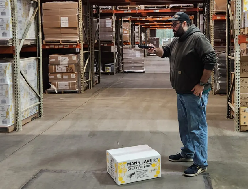 A Mann Lake employee measuring a boxed product in a warehouse aisle with the M2