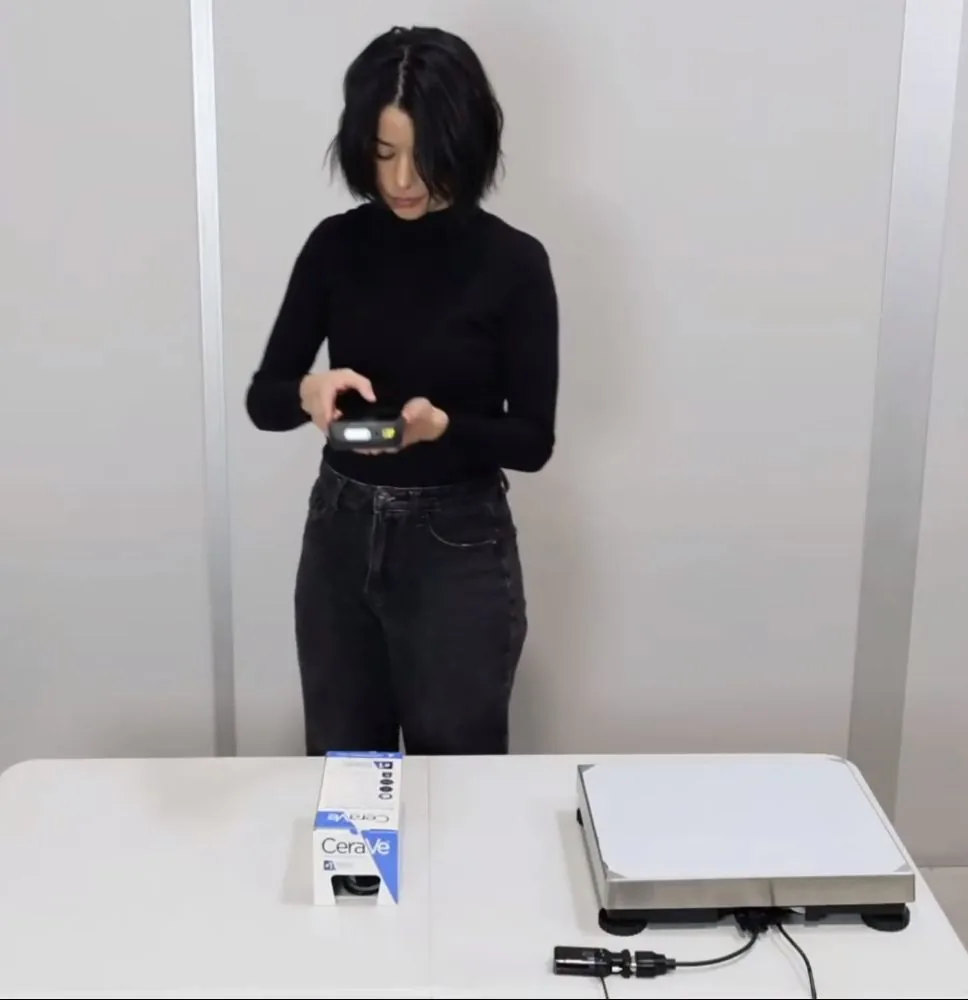 Operator at a bench measuring a boxed product with the M2, next to a scale