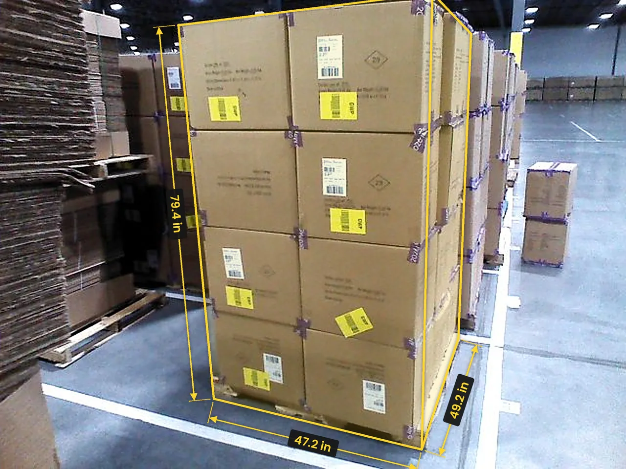 A pallet of cartons by a row of carton stacks, measured from the corner: a yellow box with length 47.2 in, width 49.2 in and height 79.4 in marked on its edges
