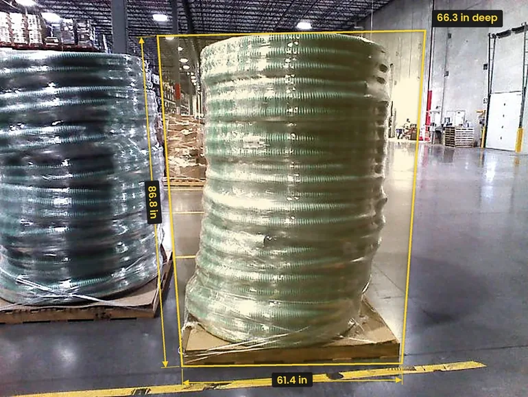 A tall coil of green hose on a pallet in a distribution center, framed by a yellow box marked 61.4 in wide and 86.8 in high