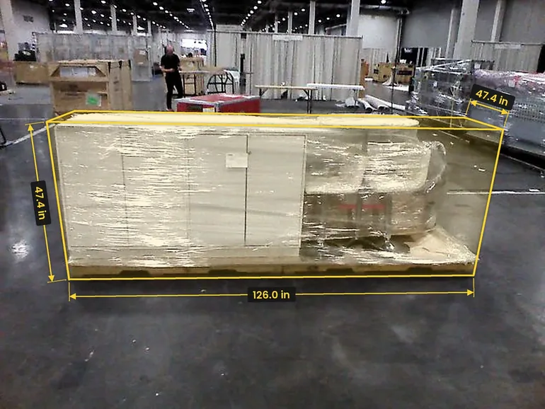 A long shrink-wrapped load on a pallet in an expo hall, framed by a yellow box marked 126.0 in long and 47.4 in high, 47.4 in deep