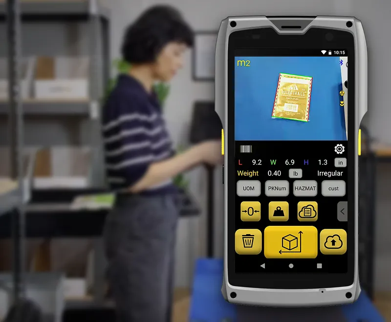 The M2 showing the Item & Parcel app result for a polybag: outlined on screen, 9.2 × 6.9 × 1.3 in, 0.40 lb, Irregular; an operator at a packing bench behind