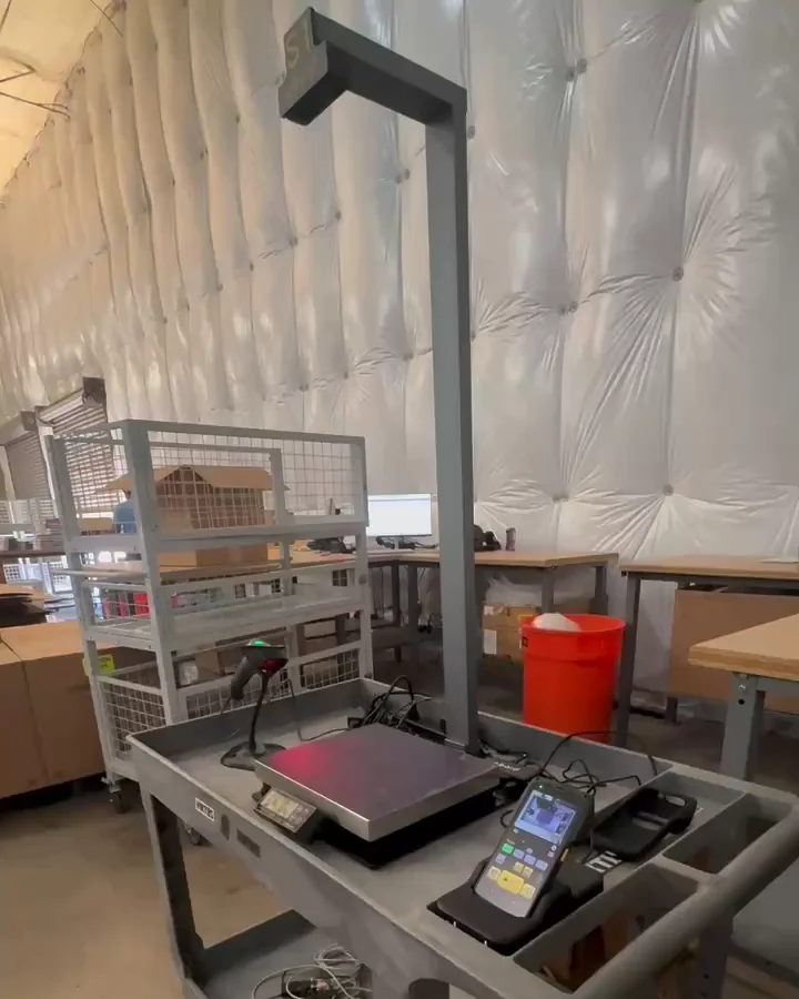 The S1 on a cart in Weby Corp's receiving area: the mast with the S1 sign over the scale, the M2 docked beside it and a barcode scanner, with receiving benches and storage carts behind